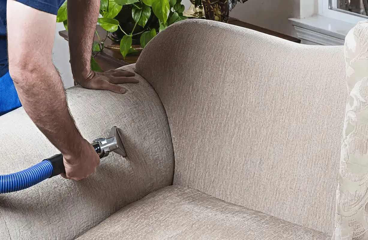Professional upholstery cleaner deep-cleaning a fabric sofa with a handheld extraction tool and hose, Columbia, SC.